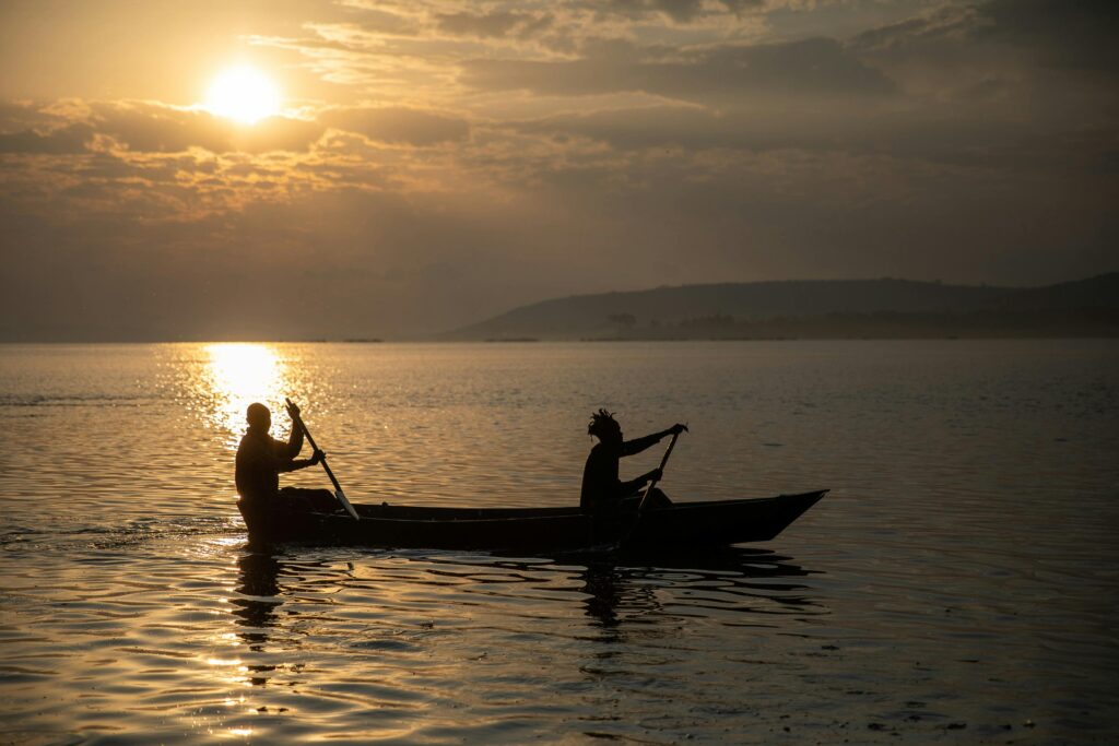 Silhouetted canoeists paddle at sunset on Lake Victoria in Jinja, Uganda.